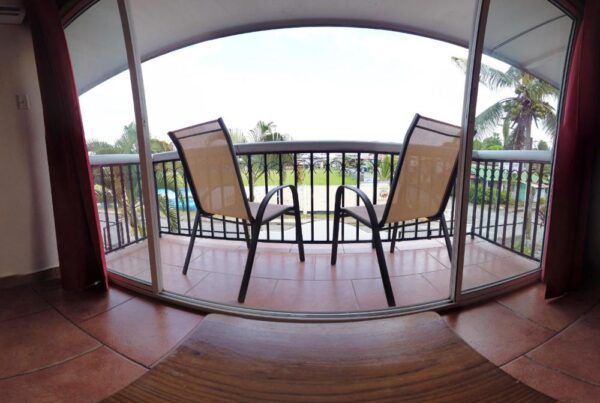 two chairs kept on a balcony with palm trees in the front.